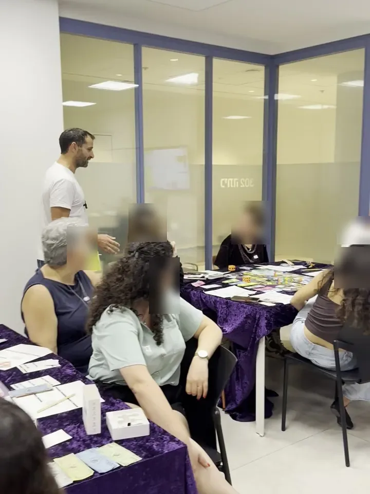 Participants sitting around a game table while Alon Bar stands beside them and guides the game